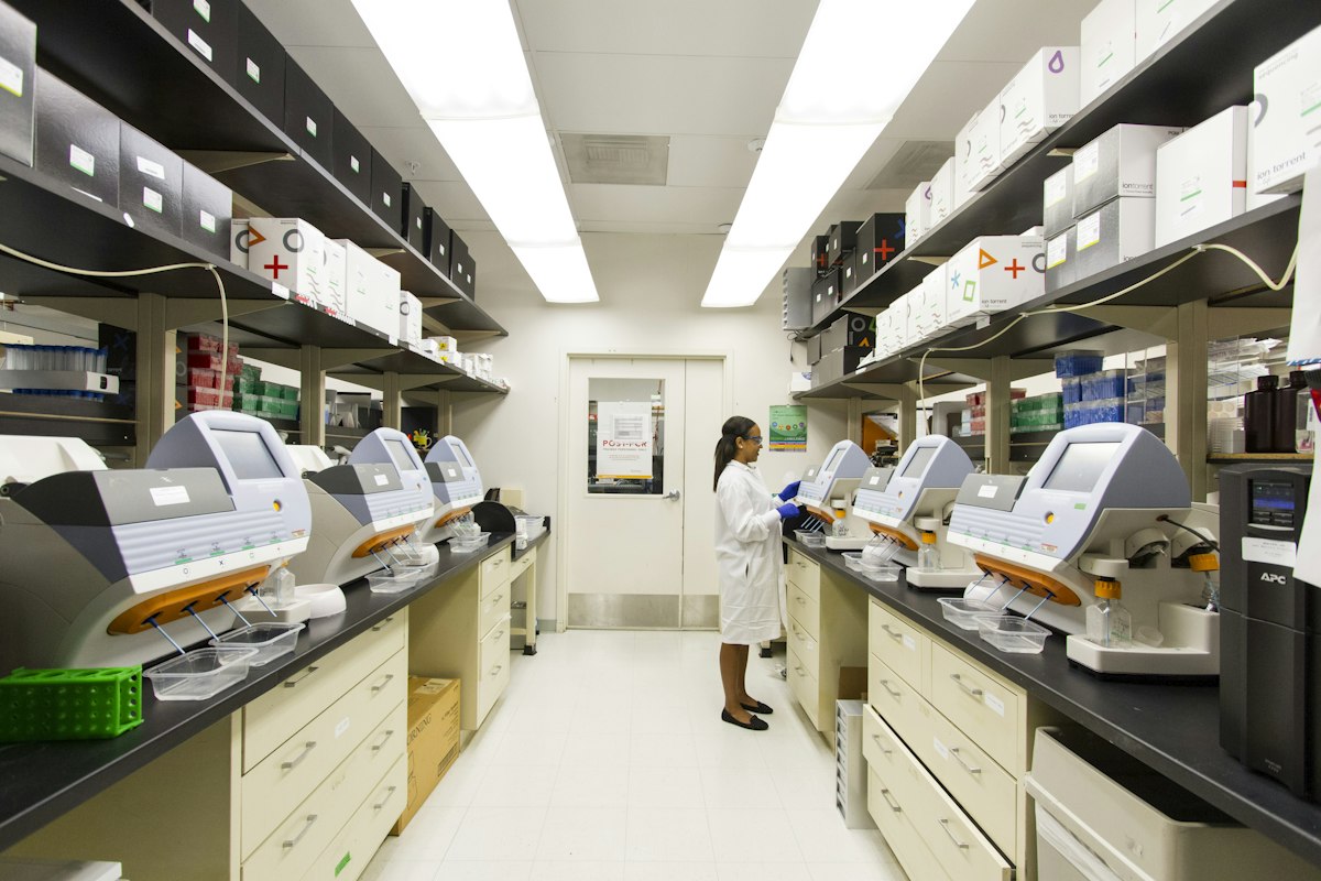 Analyst in a lab coat working between rows of benchtop instruments